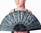 Person holding a black fan with 'MEOW' in white letters over neon outlines of cats